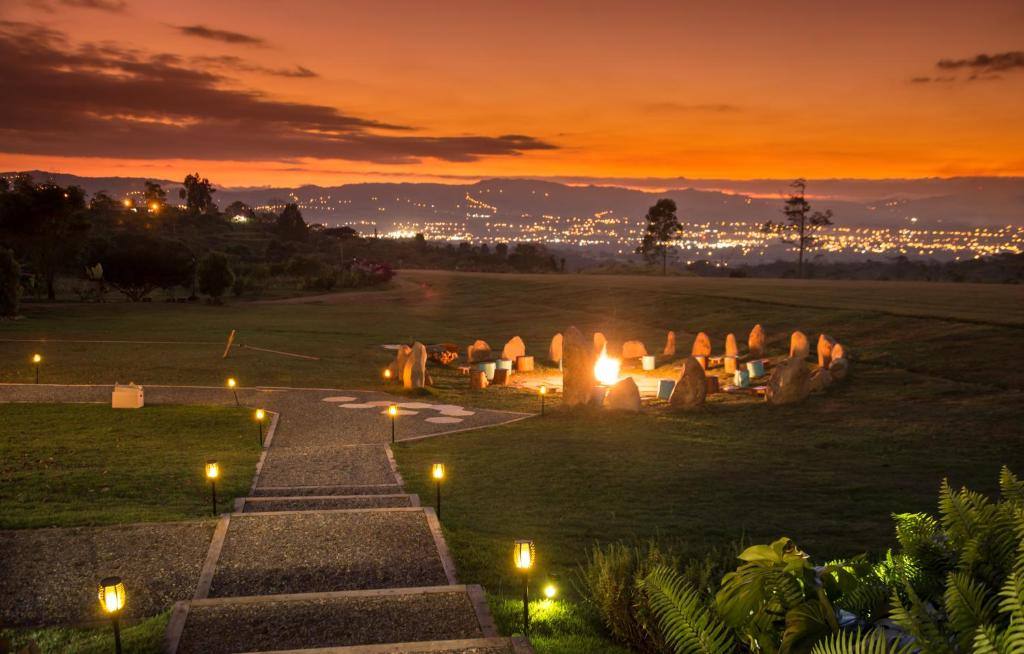 A firelit gathering circle at dusk overlooking valley lights