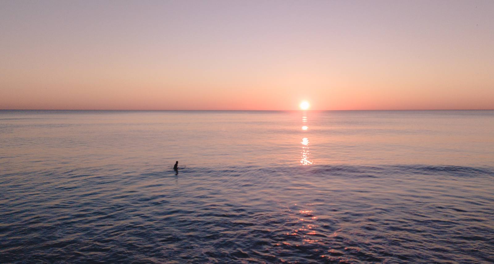 A calm pastel ocean sunset with a lone swimmer