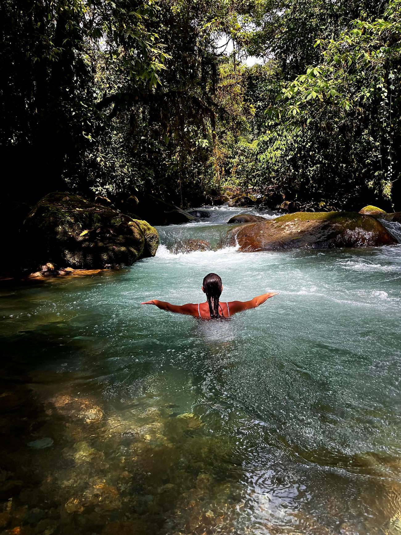 A traveler immersed in a turquoise jungle river, arms open