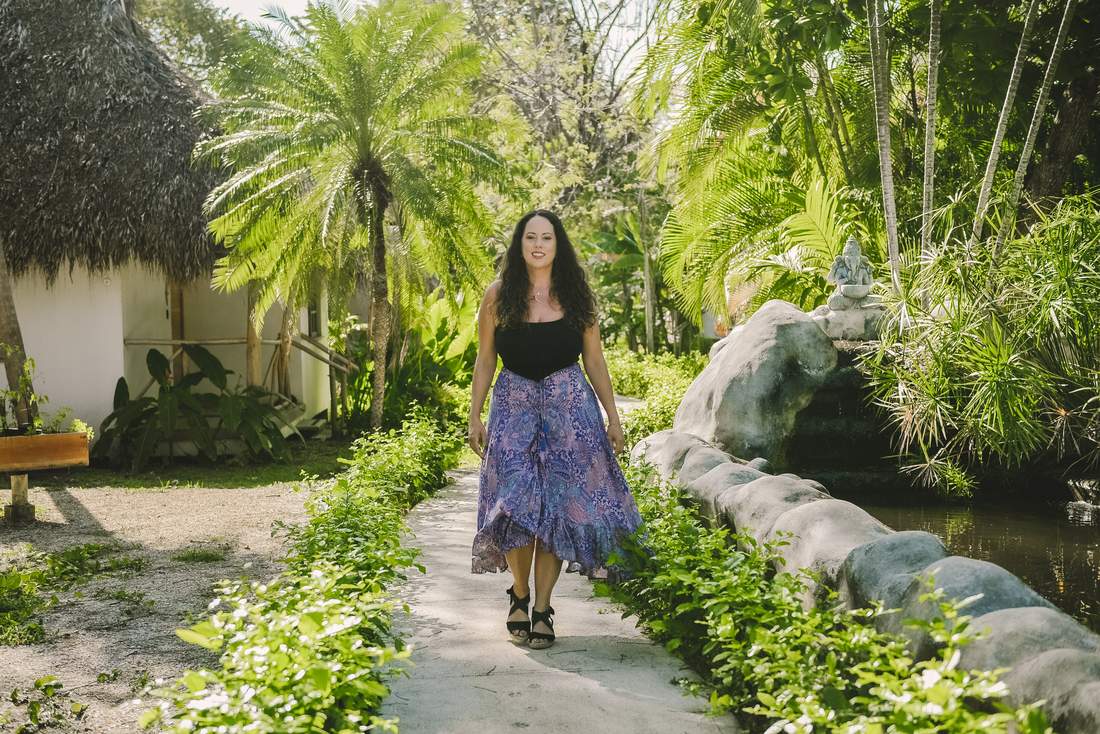 Sara walking a garden path between palms and a thatched casita